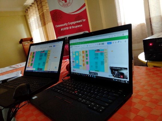 2 laptops on a table with a red cross banner in the background. The screens show how the virtual white board (Miro board) were set up.