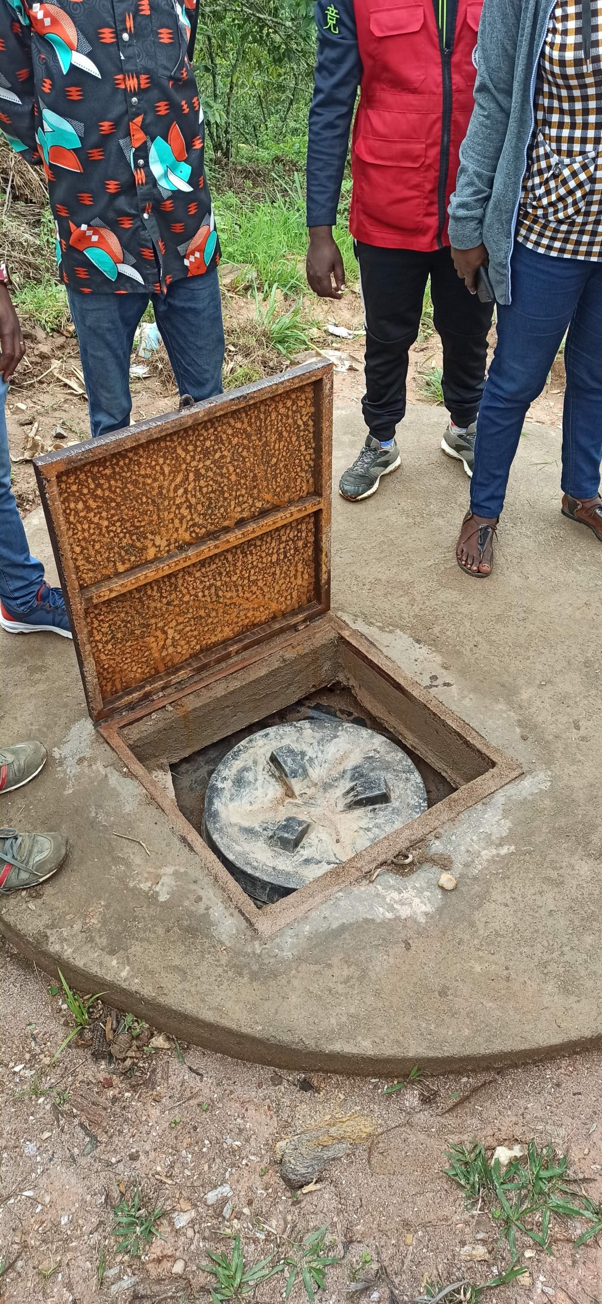 round structure made of concrete with an opening showing the access to the undergroudn storage tank. 4 people standing around the opening of the tank, the photo shows only their legs and feet